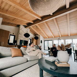Modern living room with wooden beams and a woman using a laptop.