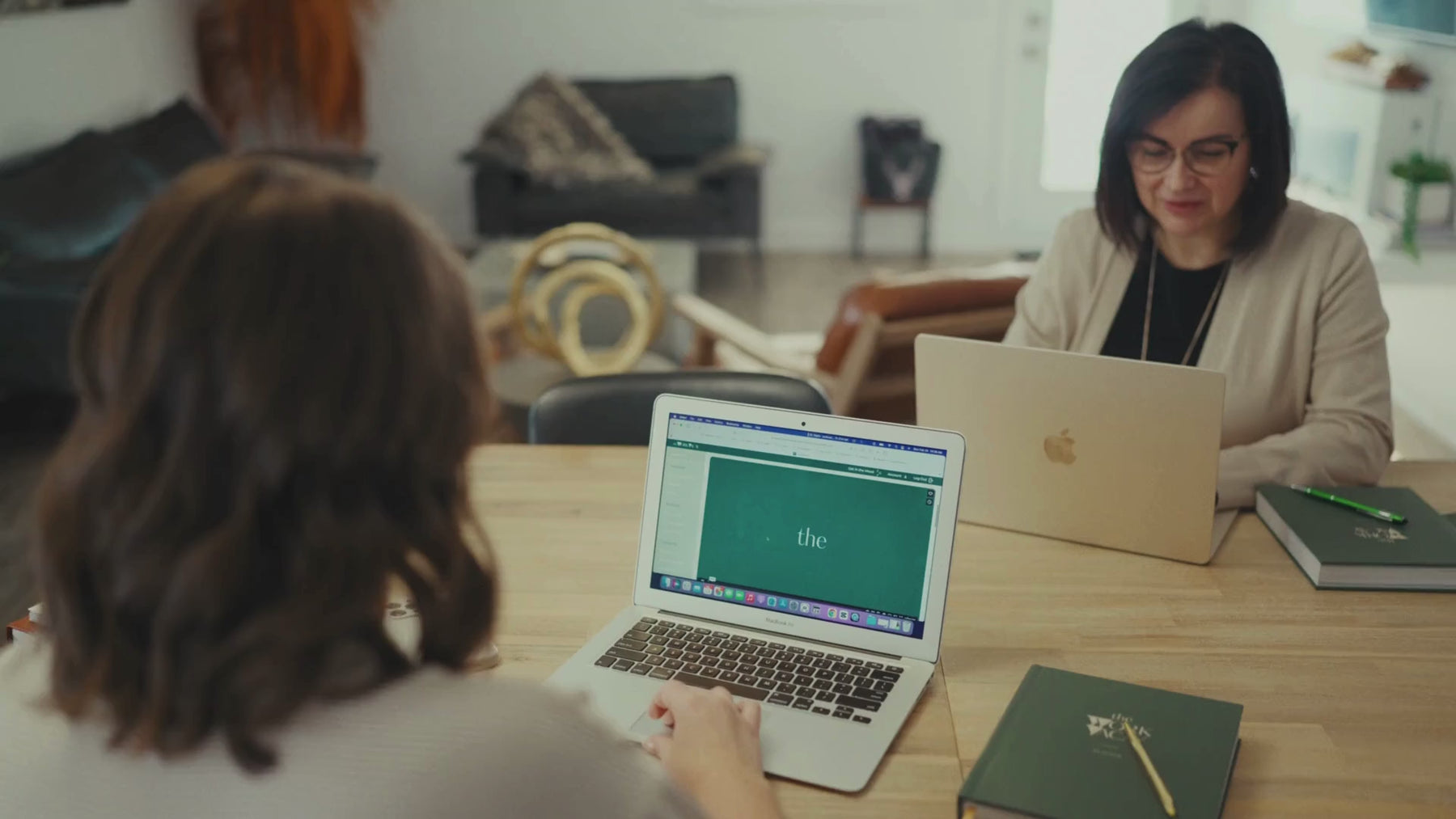 Two women sitting at a wooden table exploring The Work VACAY website.
